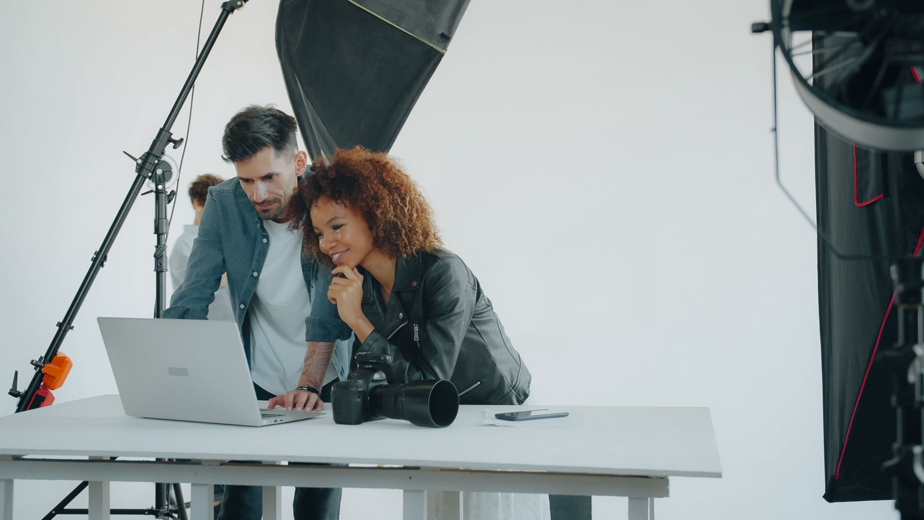 Two photographers reviewing work on a laptop in a professional studio setting.
